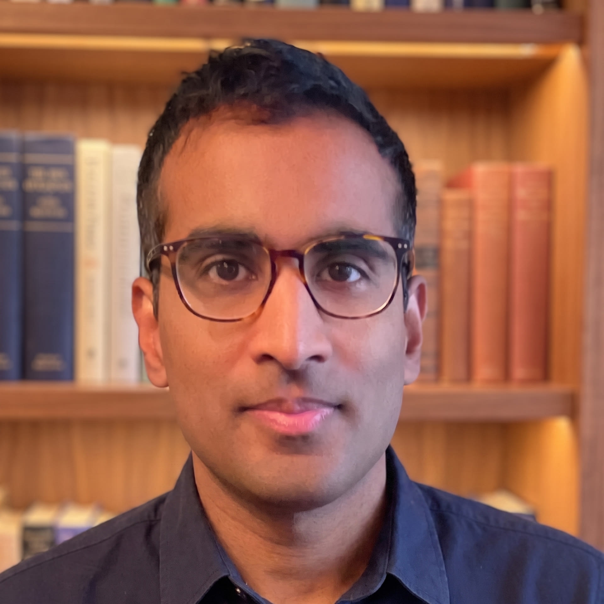 Robin Joseph, Portrait vor einer Bücherwand, dunkelblaues Hemd